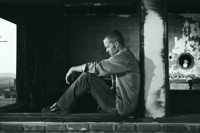 man sat in black and white room looking forlorn